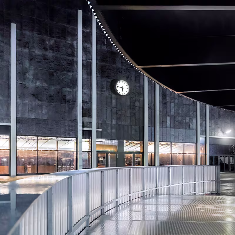 Moderne, geschwungene Fassade des Theater am Großmarkt in Hamburg bei Nacht mit großer Uhr und beleuchtetem Foyer