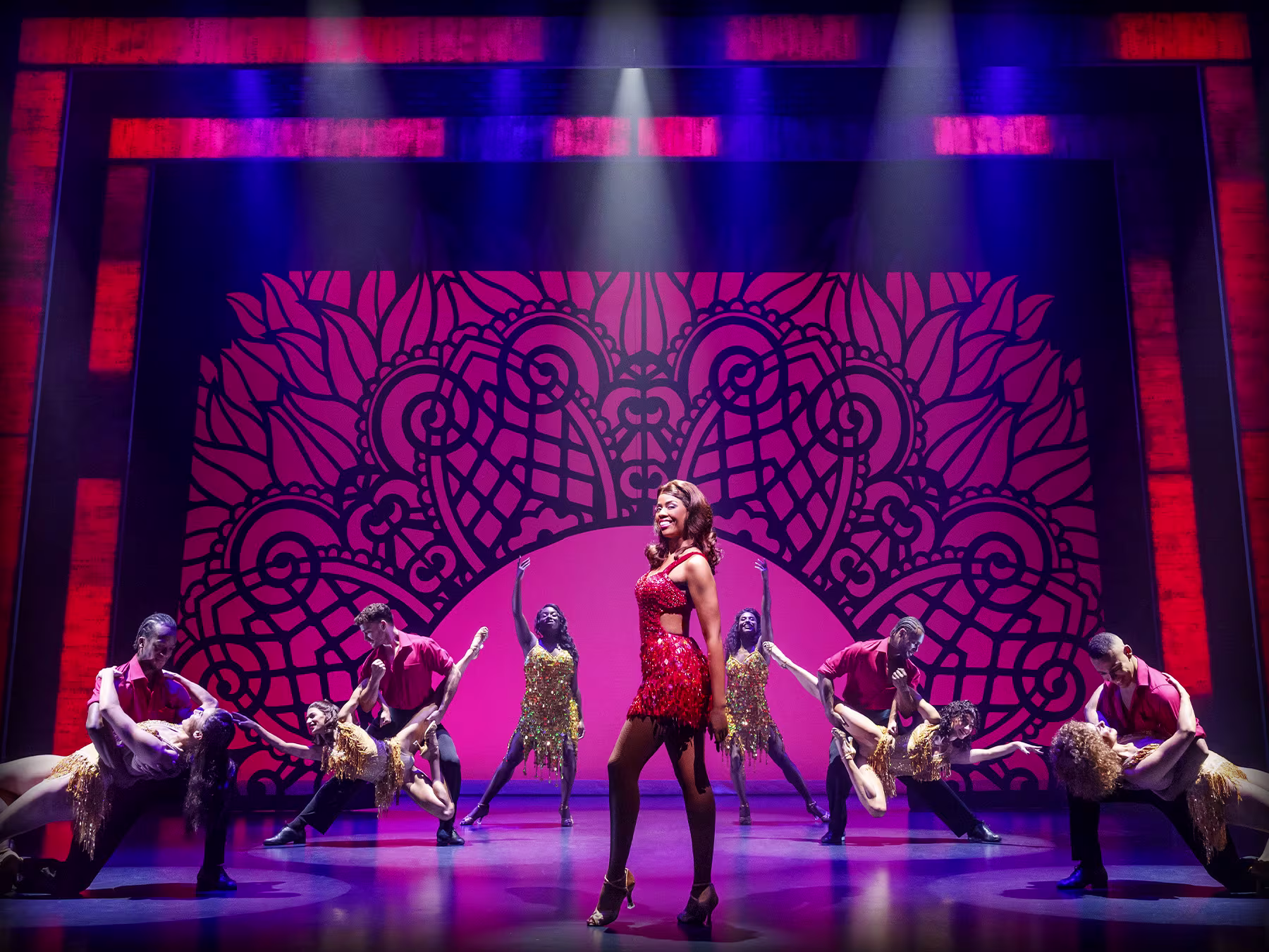 "The Bodyguard – The Musical": Darsteller*innen in rot-schwarzen und goldenen Kostümen tanzen auf der Bühne vor rot-blauem Hintergrund