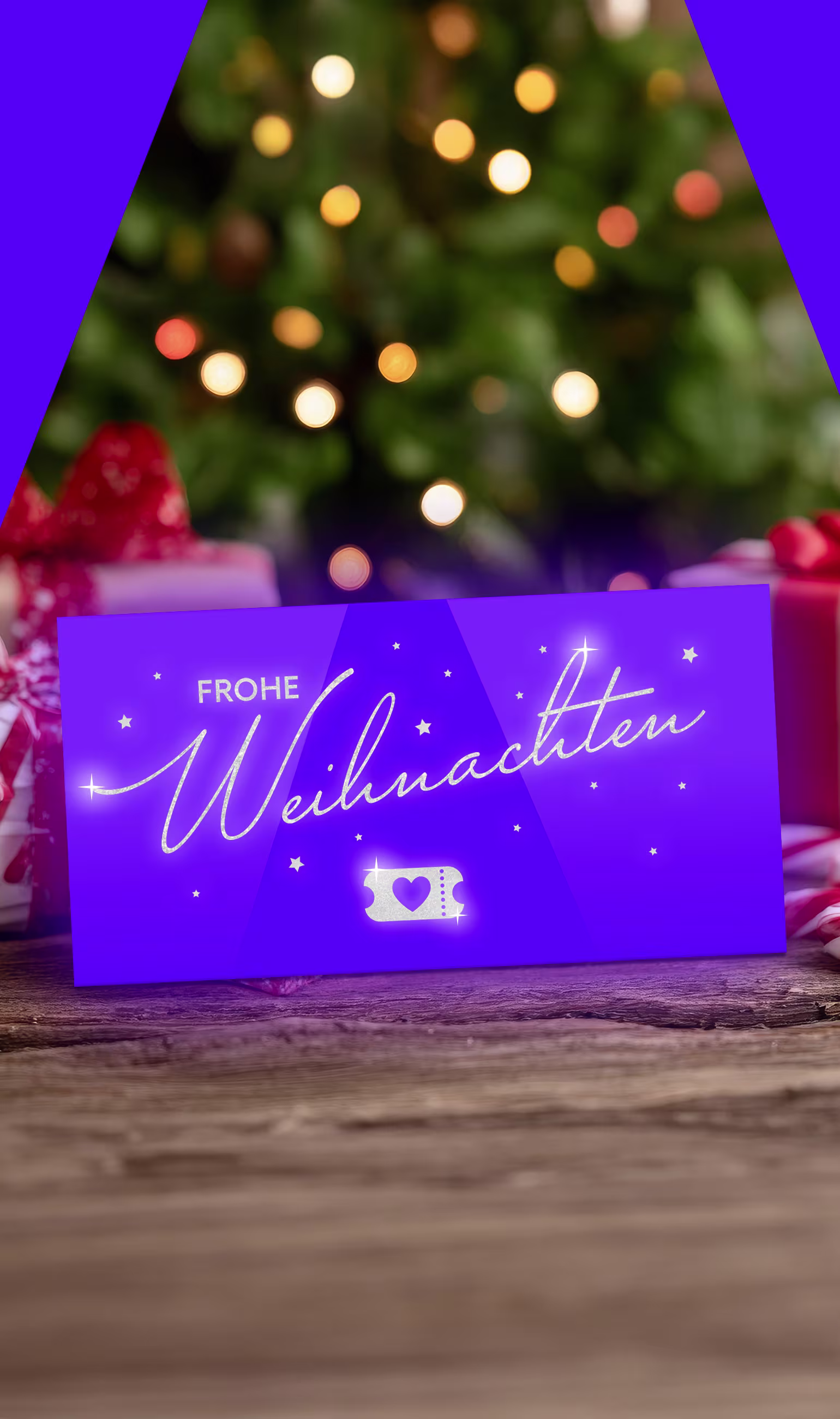 Geschenke liegen im Hintergrund vorn einem Weihnachtsbaum und vorne ist eine lila Geschenkgutschein auf dem Frohe Weihnachten steht