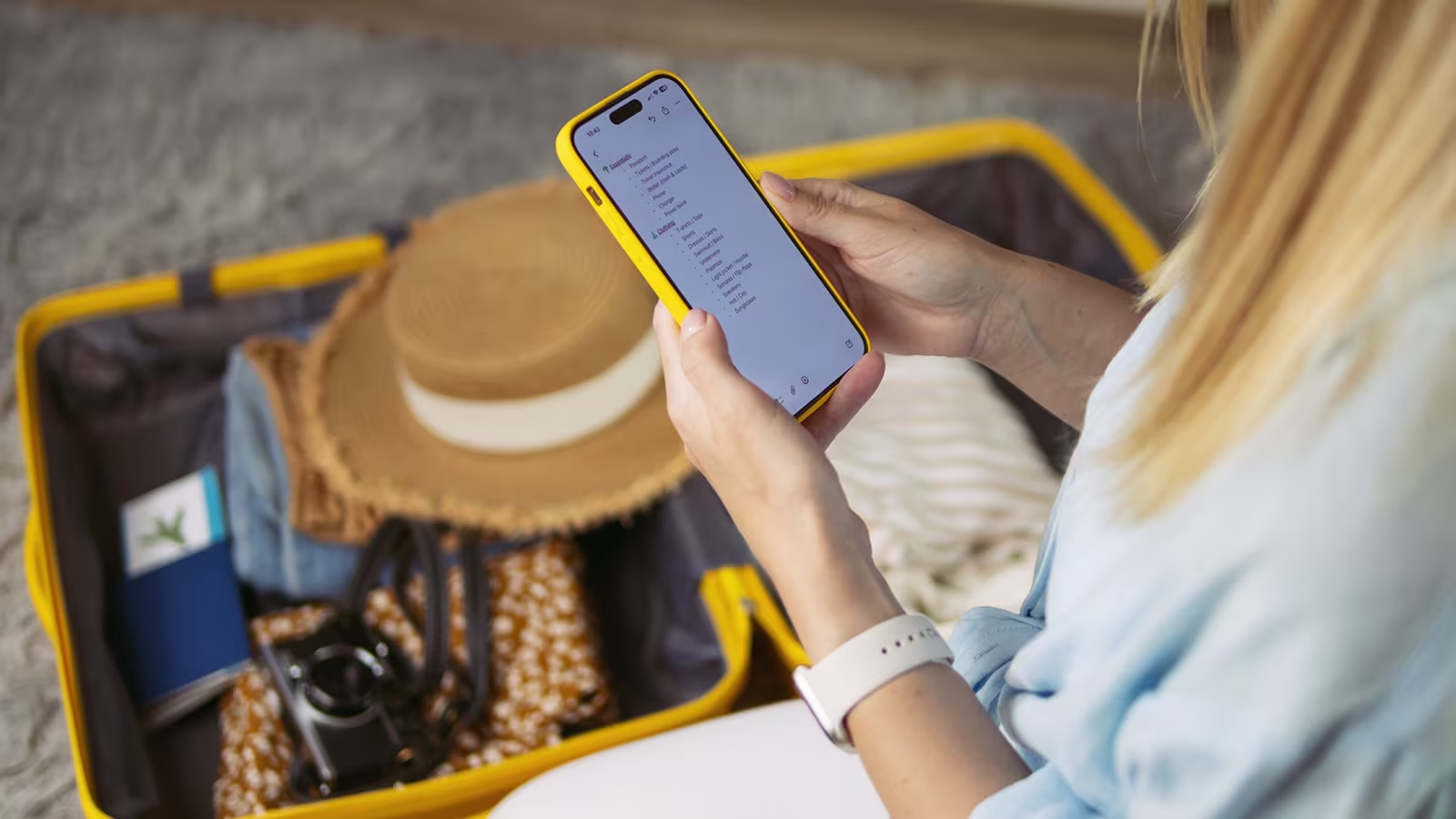 Frau packt ihren Koffer und prüft die Packliste für den Mädelstrip auf dem Smartphone