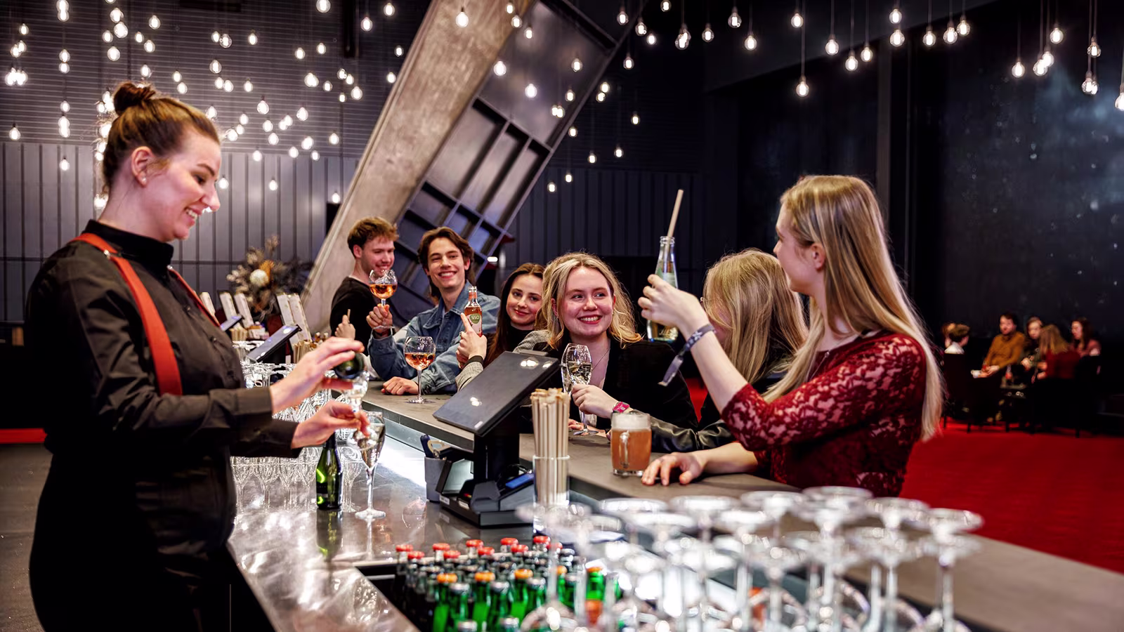 Mehrere Personen sitzen an einer Bar im Theater am Großmarkt in Hamburg und trinken lächelnd Getränke.