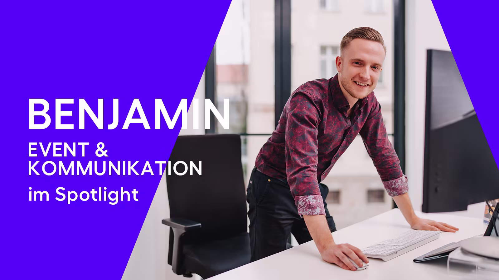 Mann mit buntem Hemd steht am Schreibtisch und lacht in die Kamera