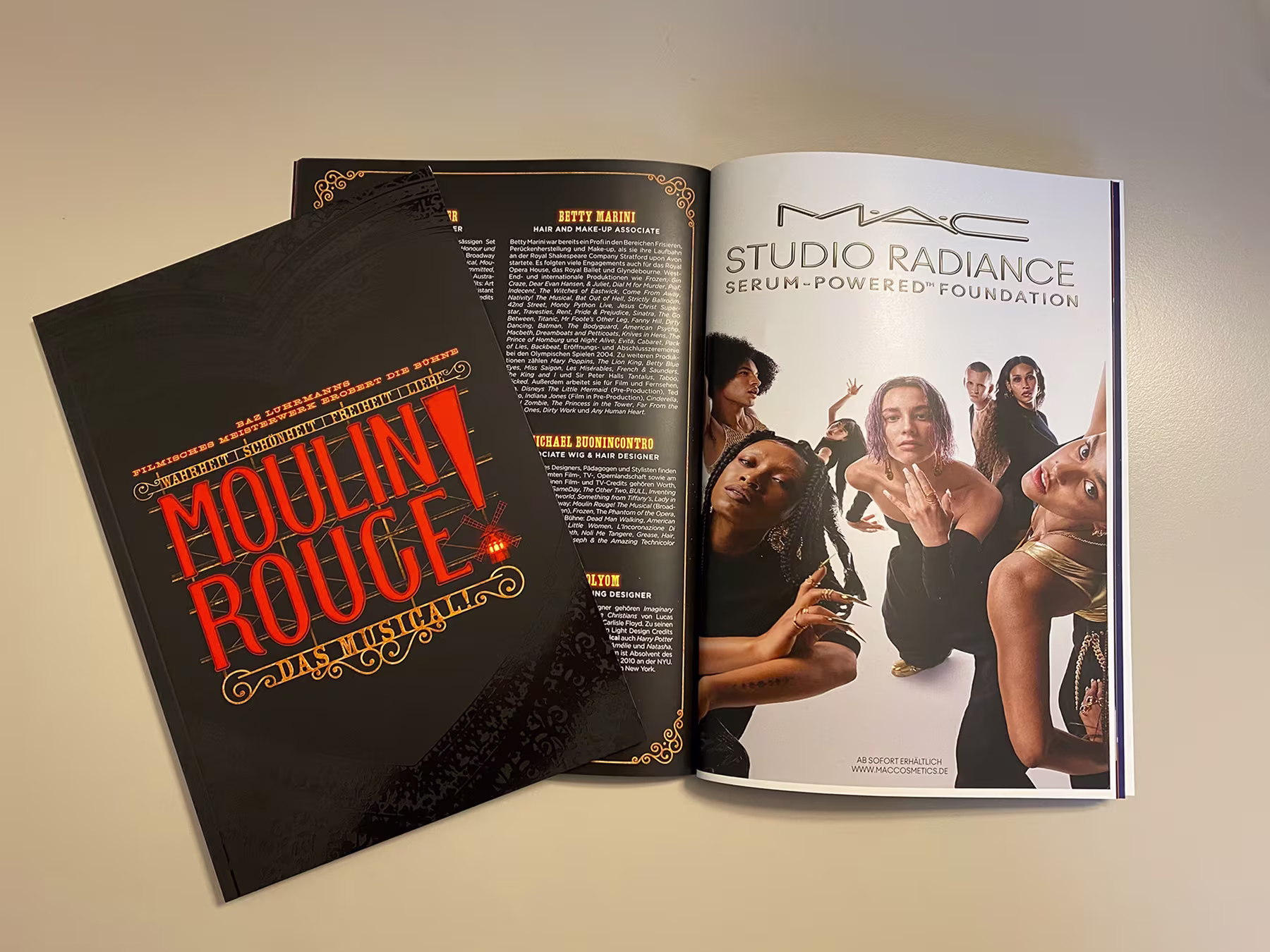 Aufgeschlagenes Programmheft von Moulin Rouge! Das Musical mit Kreativteam-Biografien neben einer MAC Studio Radiance Anzeige