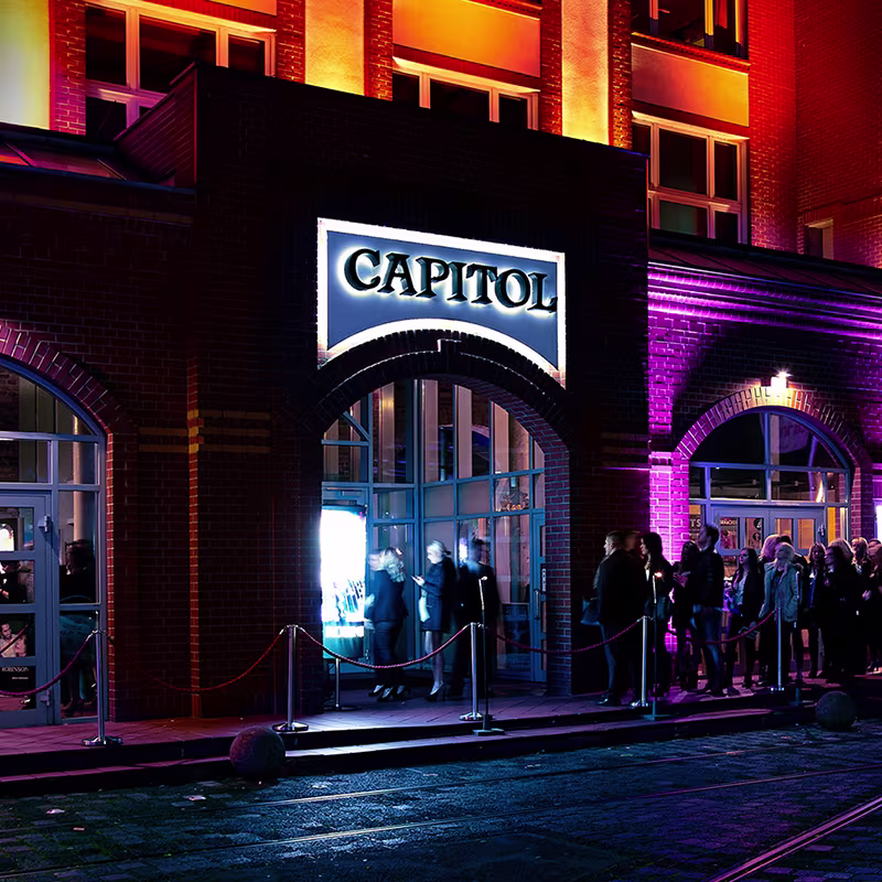 Beleuchteter Eingang des Capitol Theater Düsseldorf bei Nacht mit wartenden Gästen vor dem roten Absperrseil
