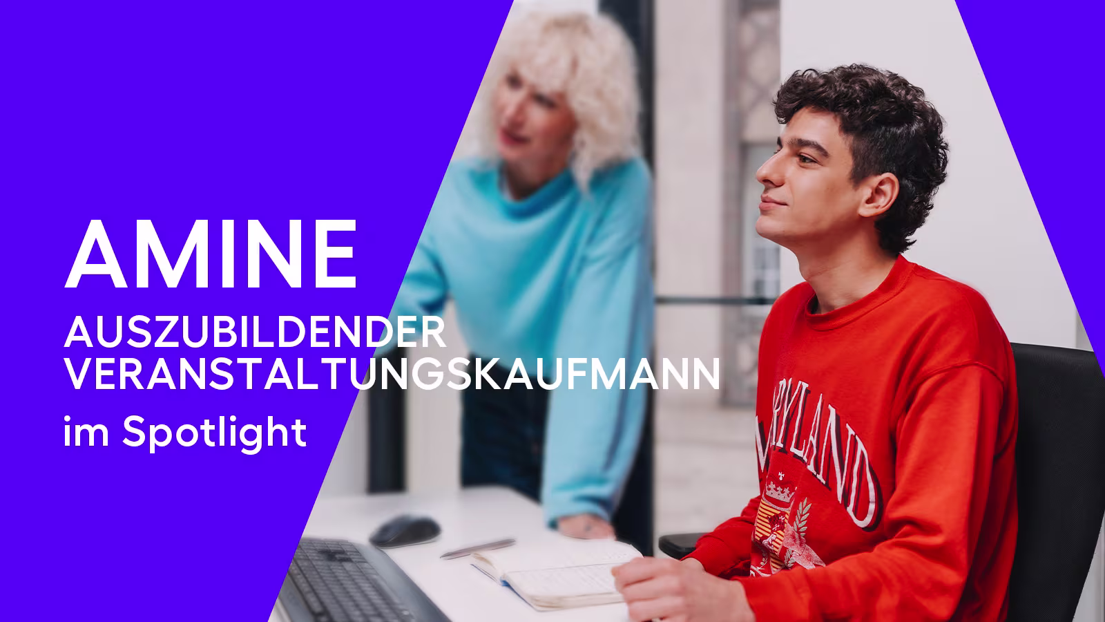 ATG Entertainment Mann mit dunklen Haaren und roten Oberteil am Schreibtisch mit Frau mit blauem Pullover und hellen Haaren