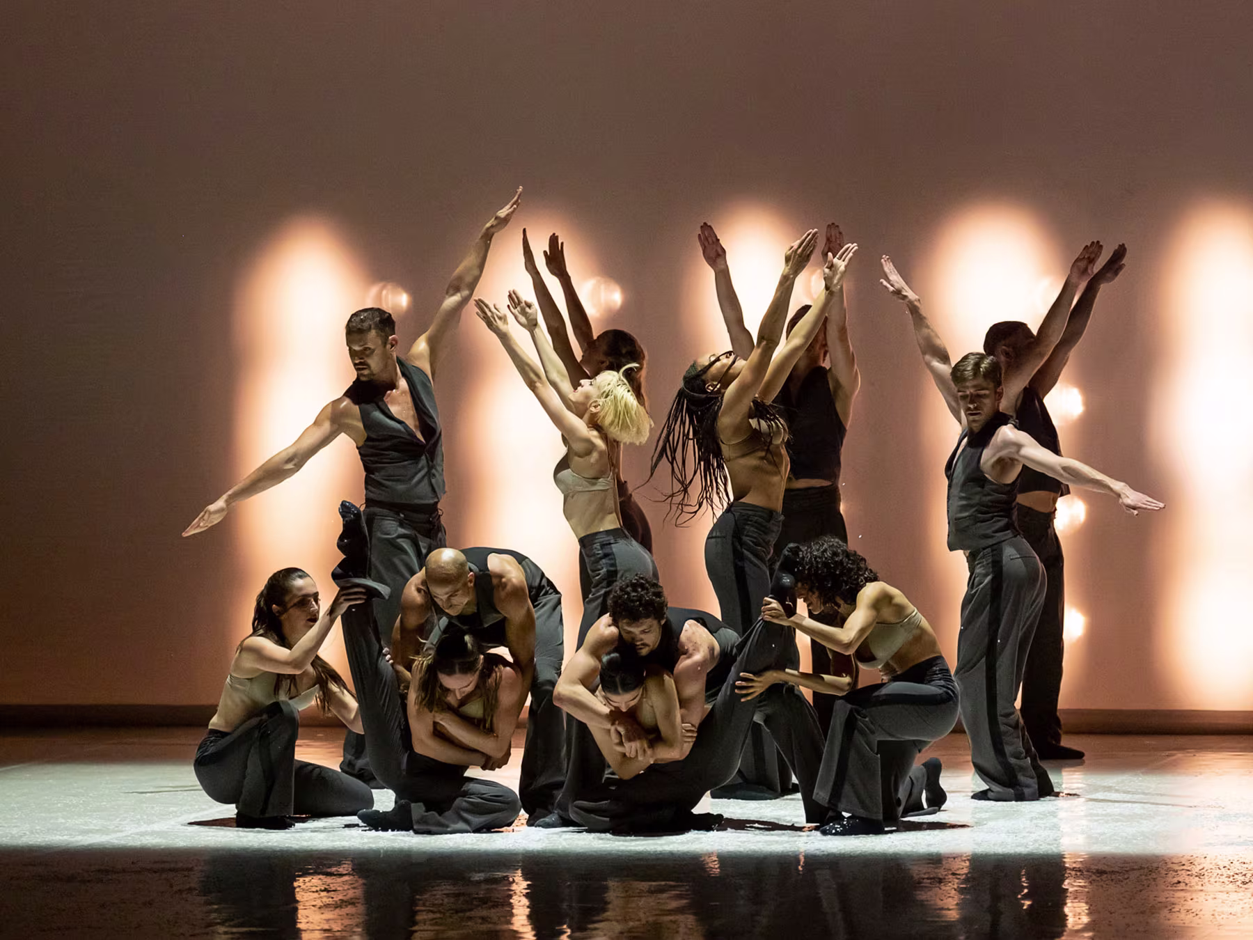 Eine Gruppe Tänzer*innen in schwarzer Kleidung bildet eine Tanzformation. 