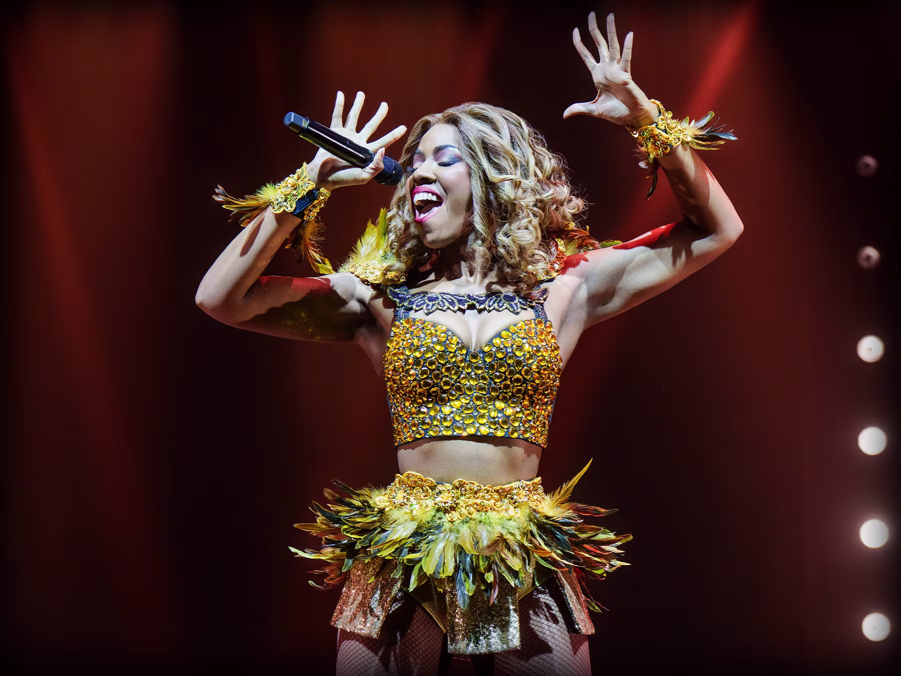 "The Bodyguard – The Musical": eine Frau in goldenem Outfit singt leidenschaftlich auf einer Bühne. 