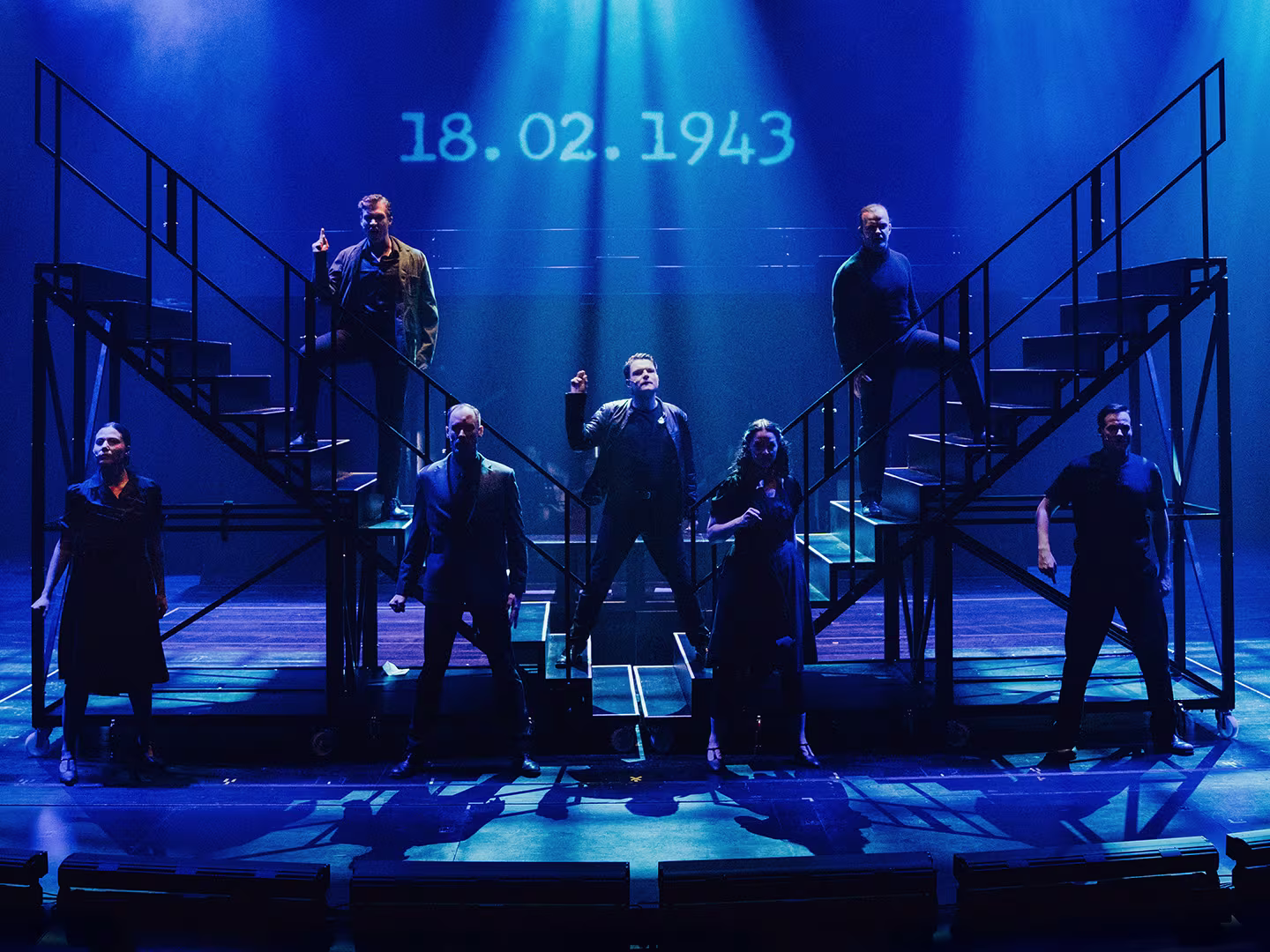 Showbild vom Musical Die weiße Rose mit einer blau beleuchteten Bühne, Personen und zwei Treppen