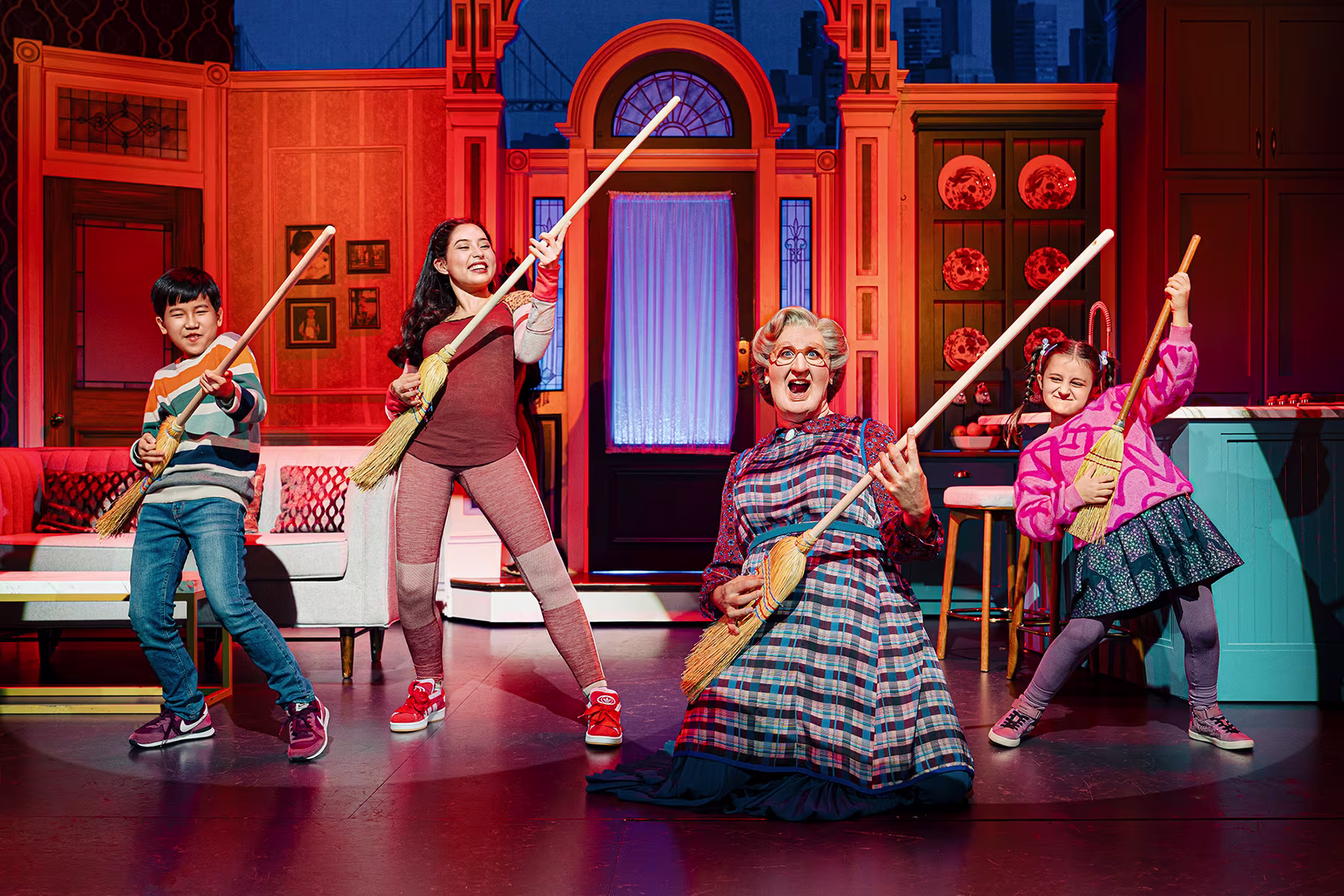 Szene aus Mrs Doubtfire – Der neue Musical-Hit: Mrs Doubtfire und die Kinder stehen auf der Bühne und benutzen Besen als Gitarre