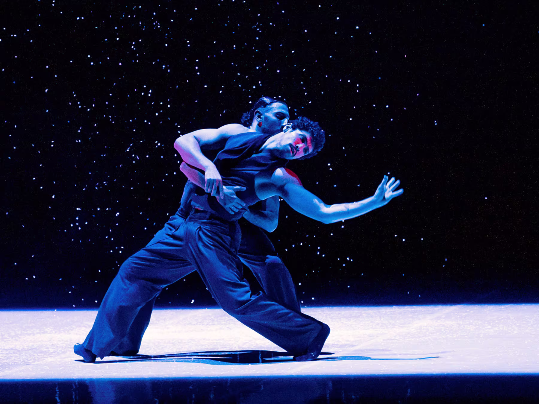 Zwei Tänzer halten sich verschlungen in blauem Licht.