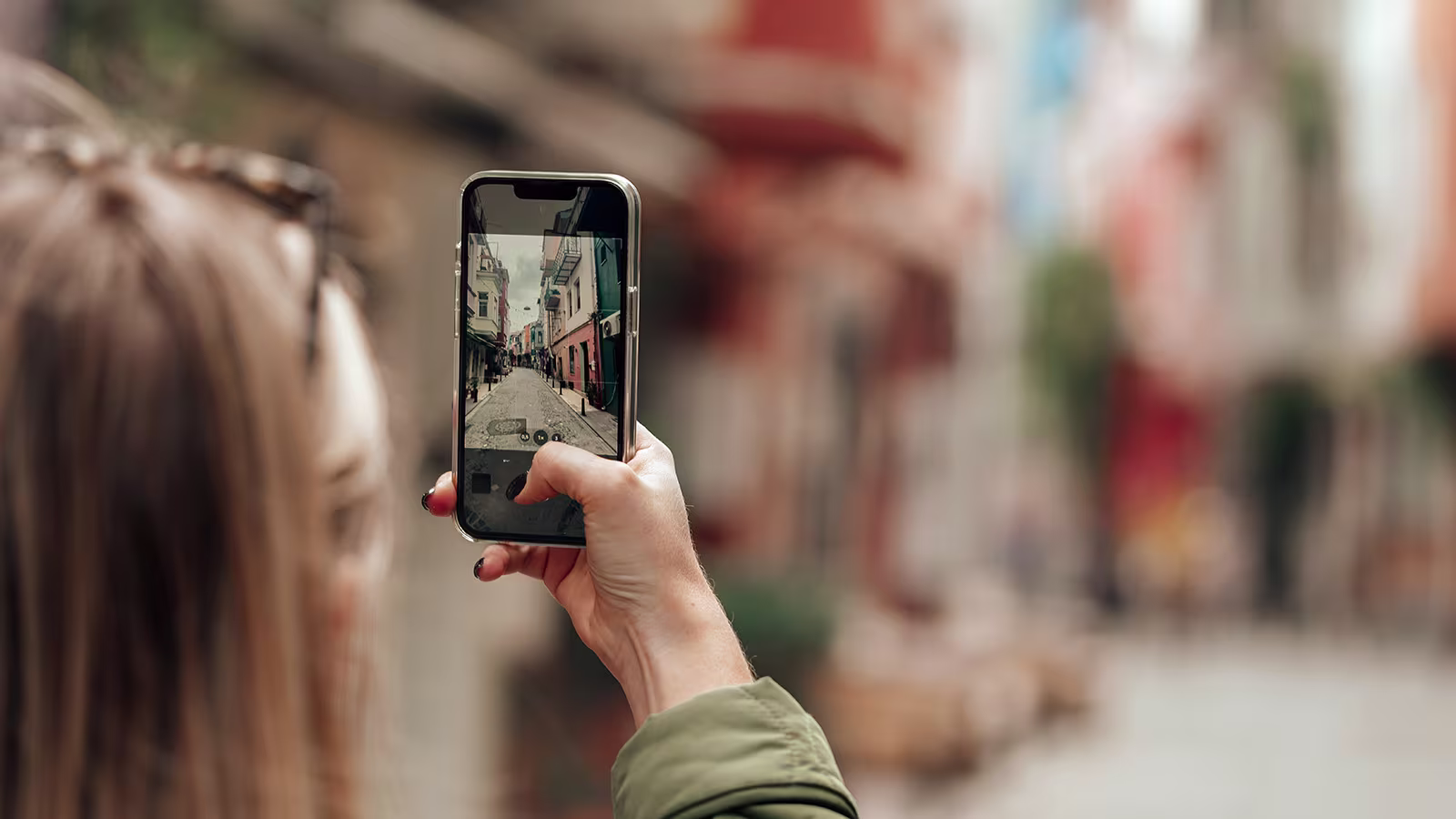 Frau fotografiert bunte Altstadtgasse mit dem Smartphone beim Städtetrip