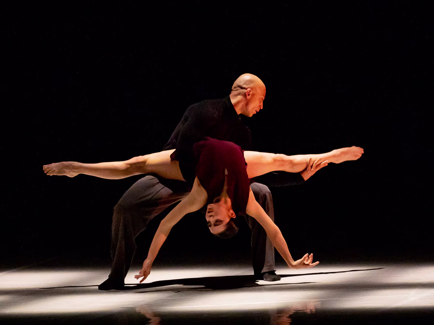Eine Frau liegt verkehrt herum auf den Beines einer Mannes der im Ausfallschritt steht. 