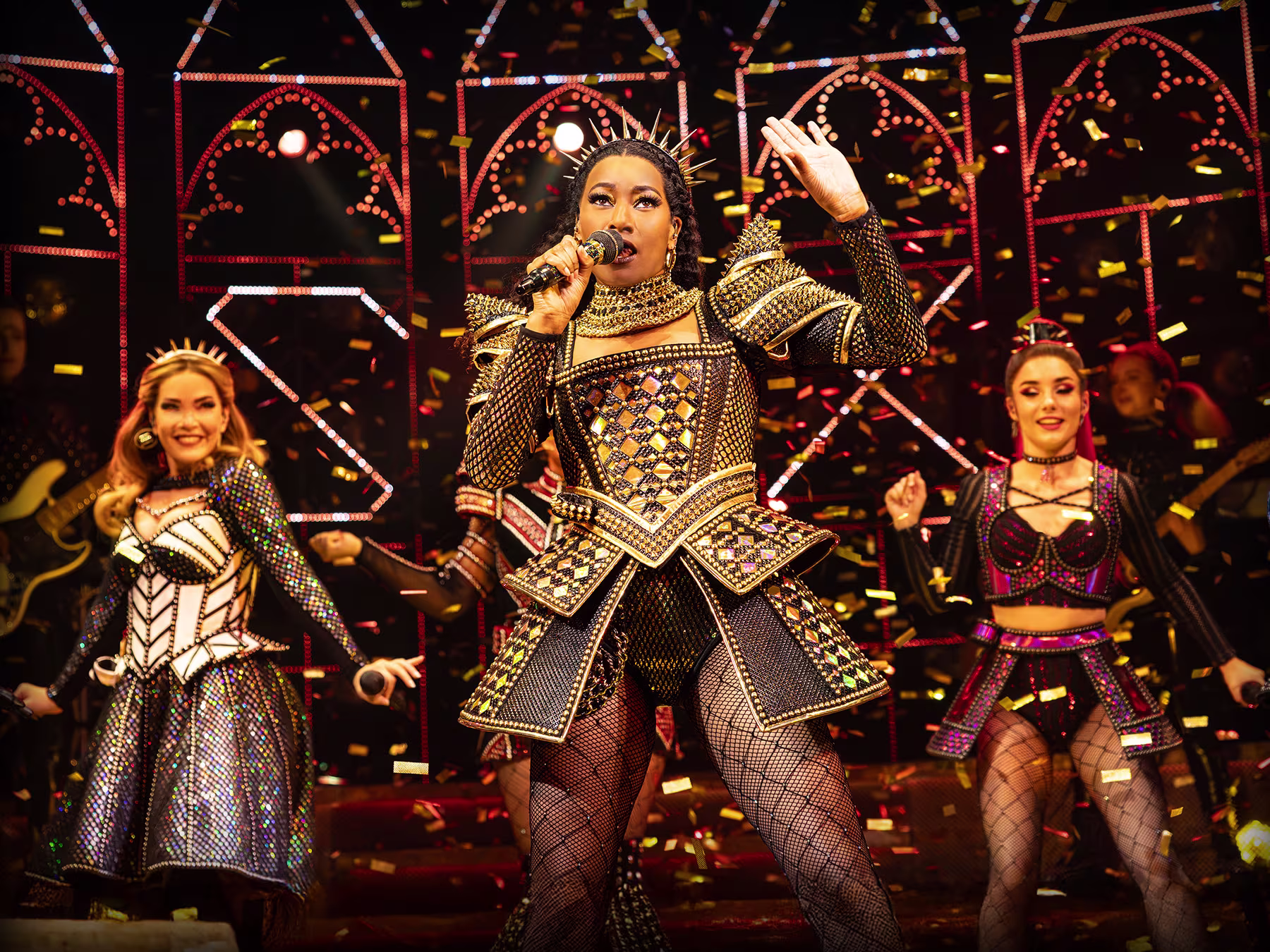 Momentaufnahme einer Szene von SIX The Musical. Die Sängerin vorne hat ein Mikrofon in der Hand und singt.