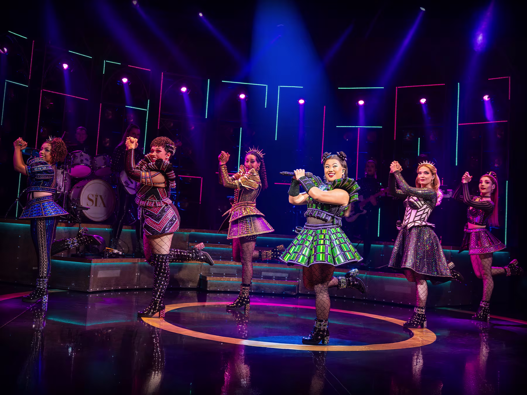 Momentaufnahme einer Szene von SIX The Musical. Die Sängerinnen haben Mikrofone in der Hand und singen auf der Bühne.