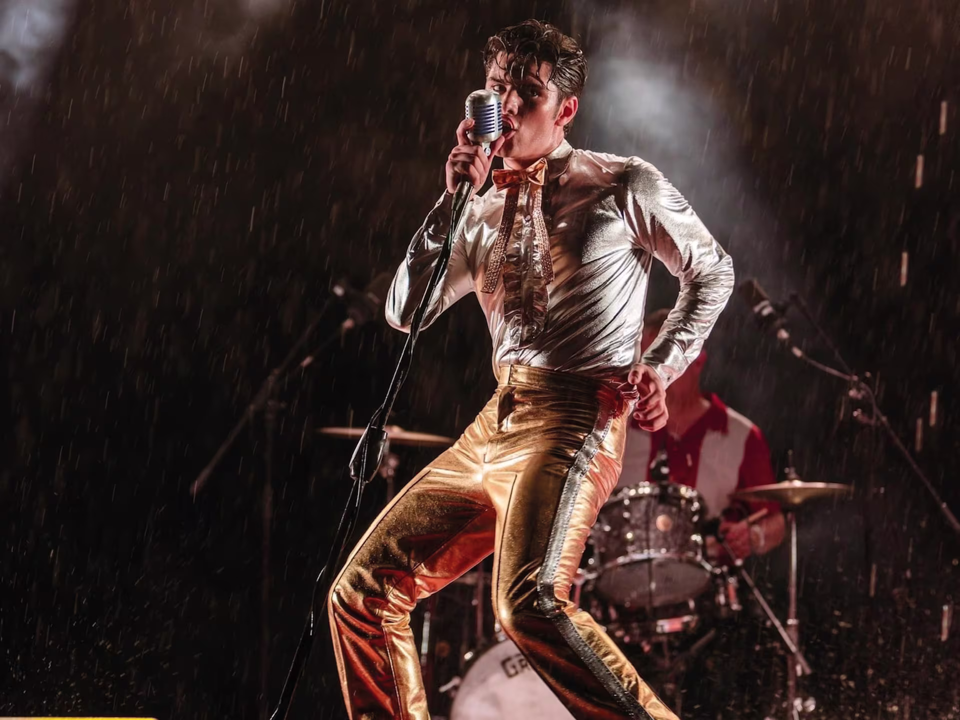 Szene aus “Elvis Tribute Artist World Tour”: Mann steht im Regen auf der Bühne und singt.