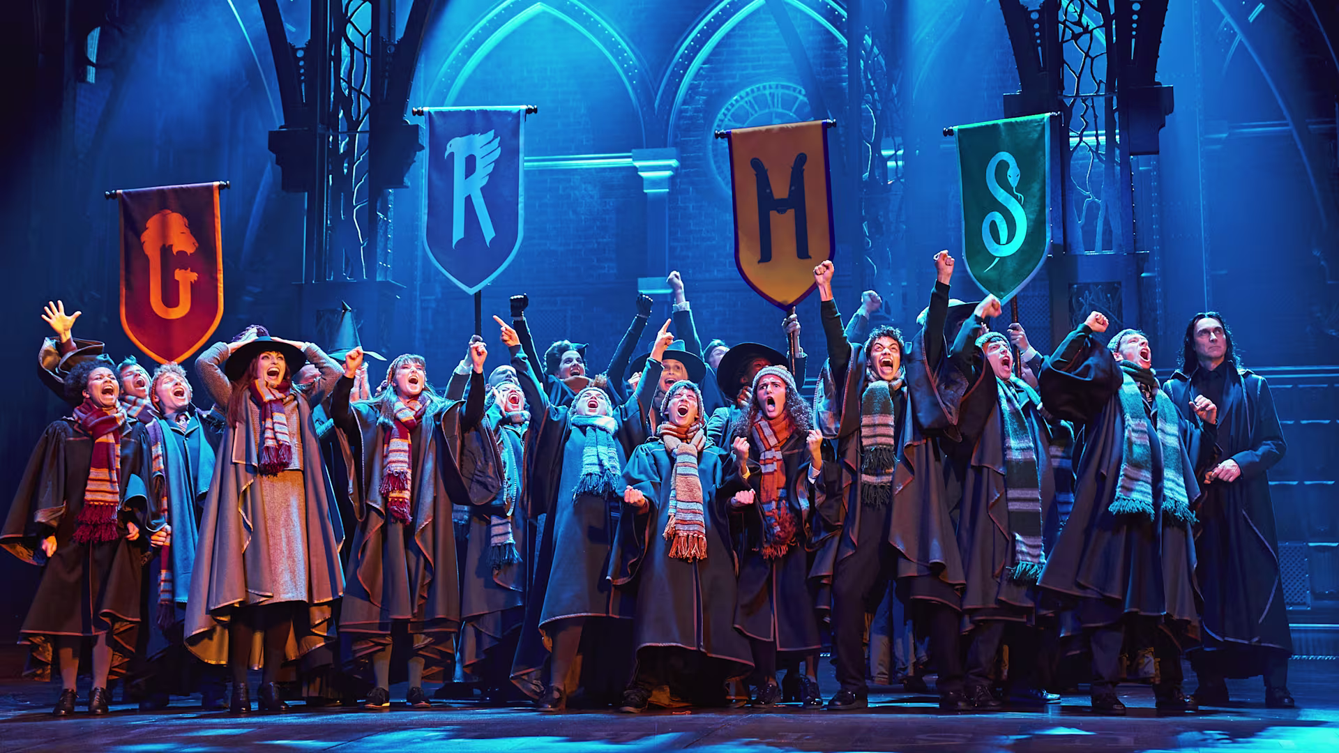 Schüler*innen aus den 4 Schulhäusern von Hogwarts jubeln auf der Bühne und stecken die Hände in die Luft.