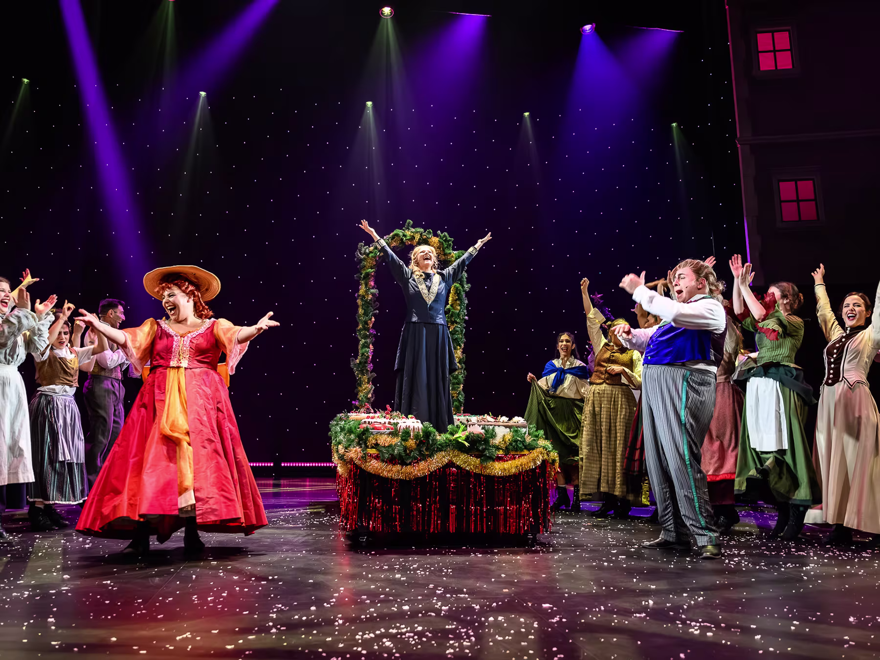 Der Geist der Weihnacht - Personen auf einer Bühne. In der Mitte zwei Frauen mit Kleidern und ein Mann. 