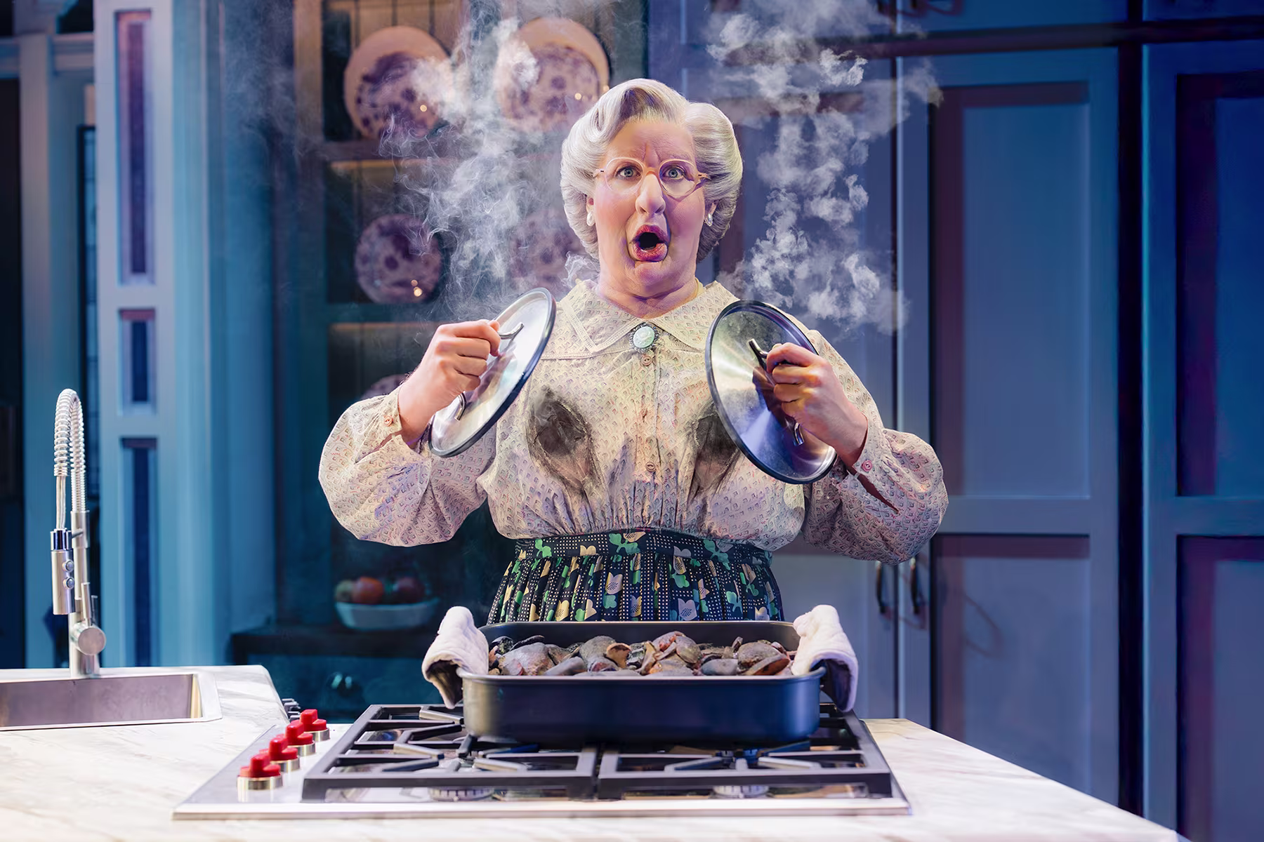 Szene aus Mrs Doubtfire – Der neue Musical-Hit: Mrs Doubtfire versucht zu kochen und verbrennt sich die Brust, dabei versucht sie das Feuer am Körper mit zwei Deckeln zu löschen.