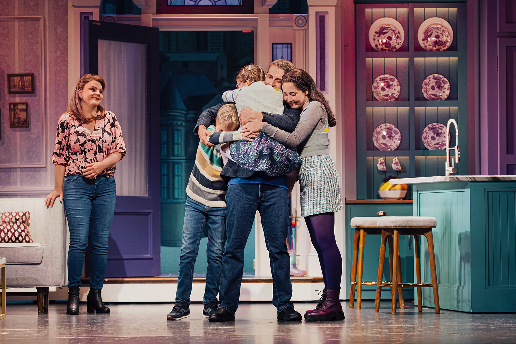 Einige Darsteller von Mrs Doubtfire – Der neue Musical-Hit blicken in die Kamera. Der Hauptdarsteller umarmt seine Kinder.