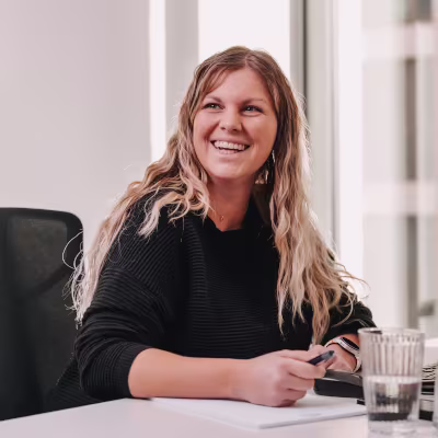 Frau mit blonden Haaren, lachend am Schreibtisch