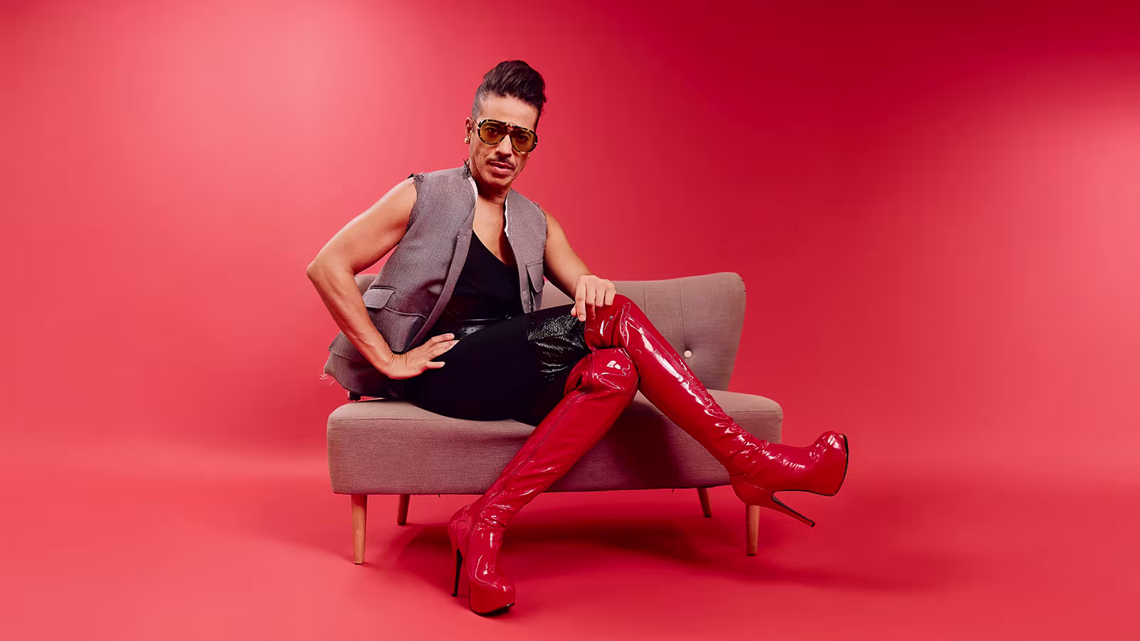 Jorge Gonzalez sitzt auf einem Sessel mit roten Overknee High Heels aus Kinky Boots Musical
