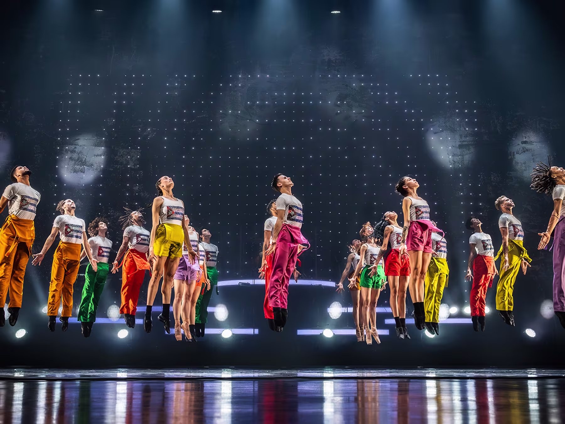 Ballet Revolución Tänzerinnen und Tänzer sind mit bunten Outfits auf der Bühne und springen hoch