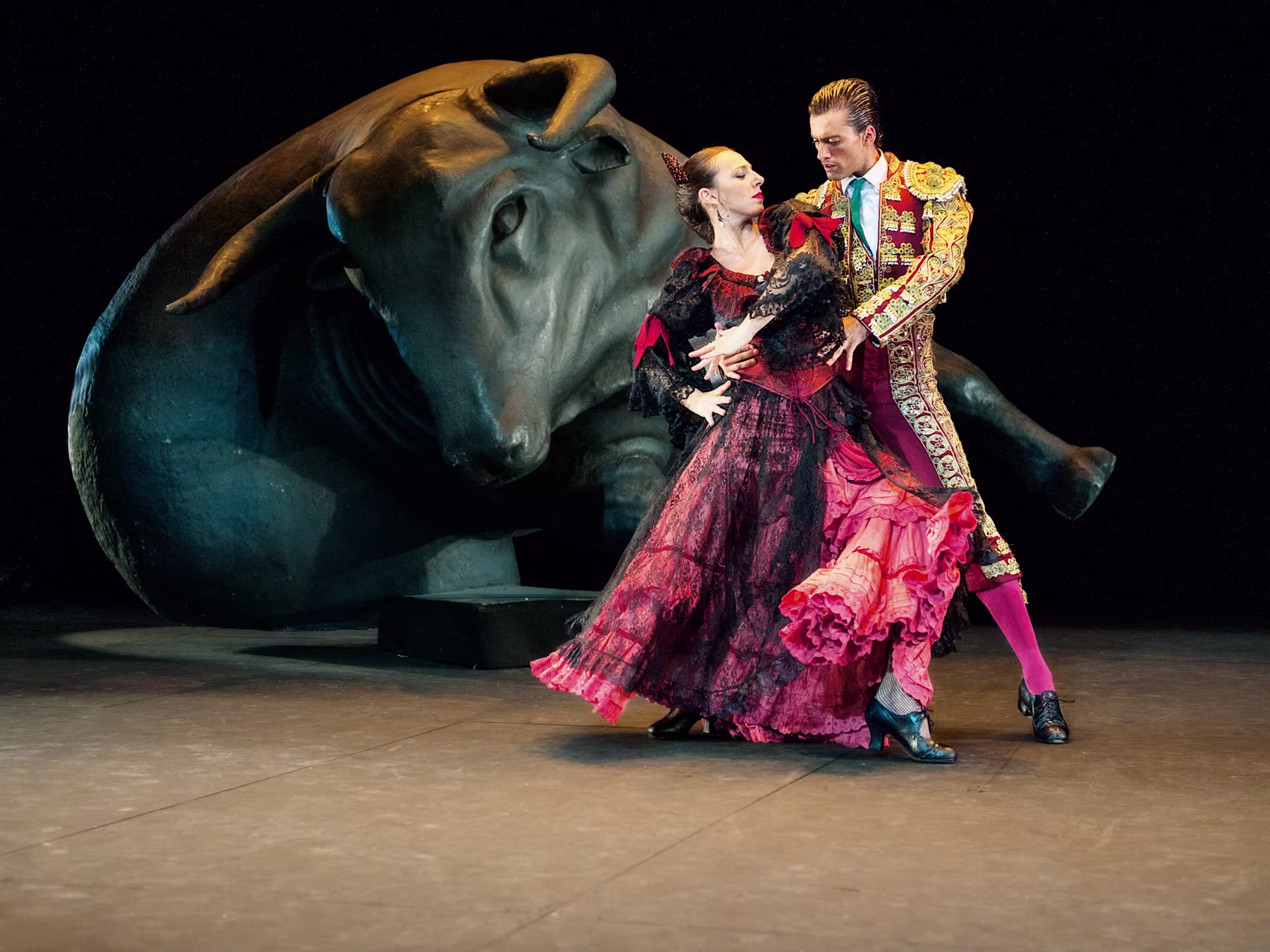 Szene aus "Carmen Flamenco": Paar tanzt auf der Bühne, im Hintergrund kann man einen Stier erkennen.