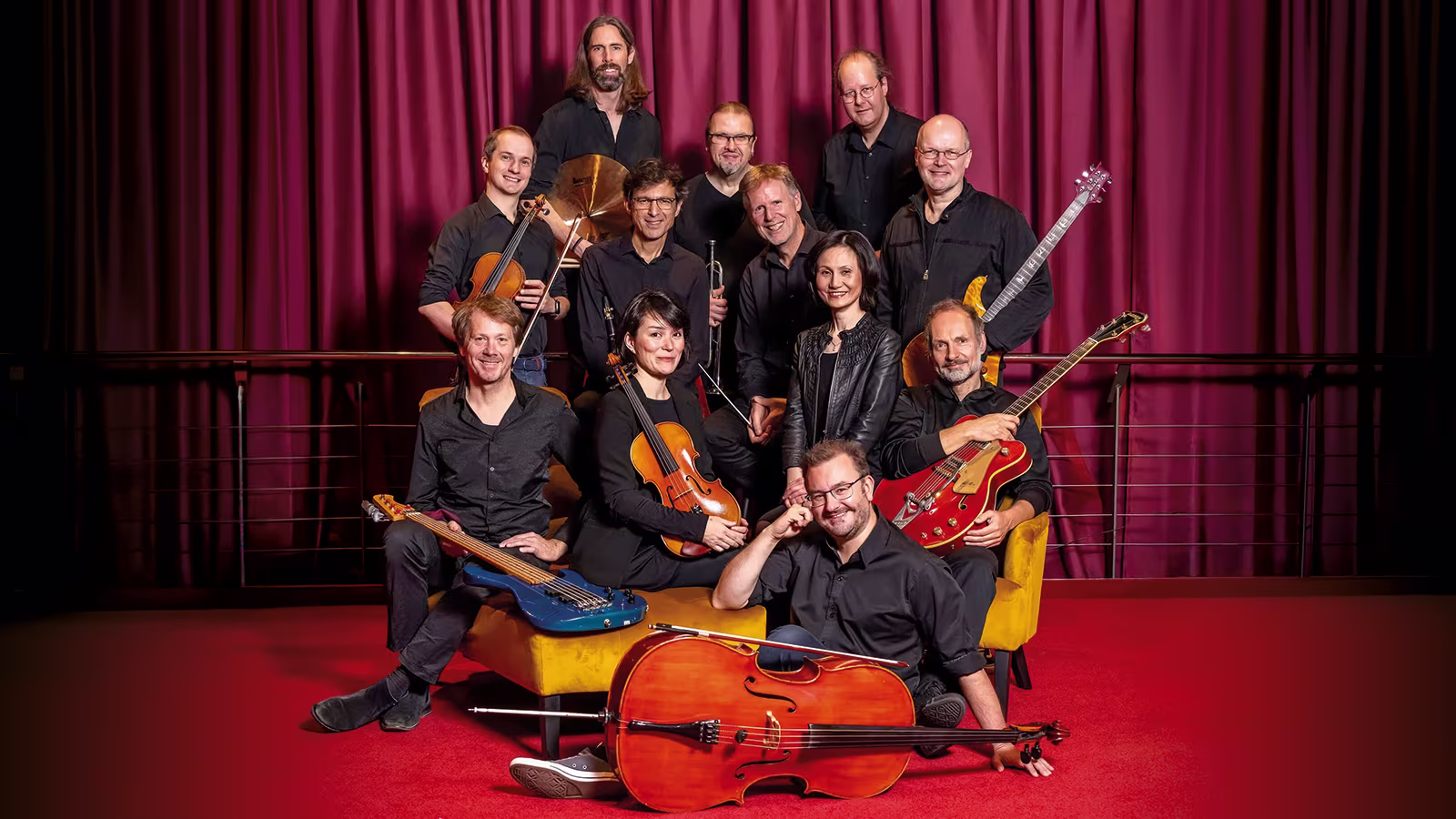 Die Band von Moulin Rouge! Das Musical posiert vor einem roten Vorhang.