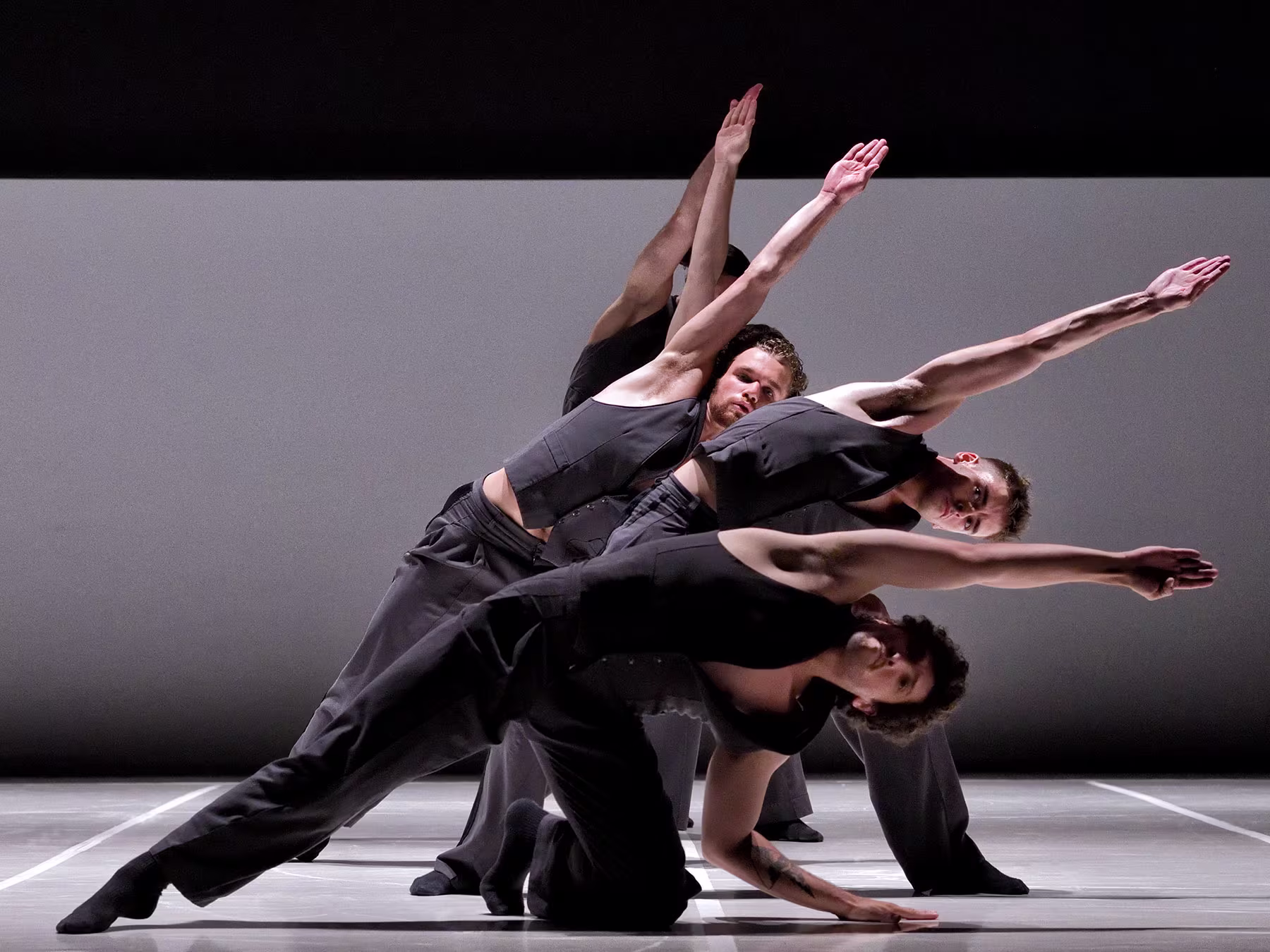 Vier Tänzer*innen in schwarzer Kleidung bilden eine Tanzformation mit gestreckten Armen. 