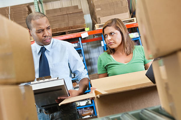 Woman opening a box in warehouse upset at man with clipboard
