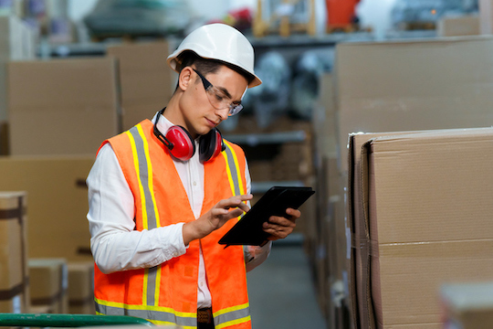 Person in hard hat reading a tablet in a warehouse