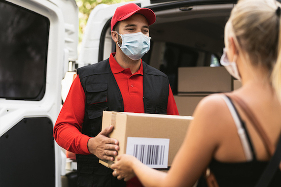 Masked delivery driver handing package over