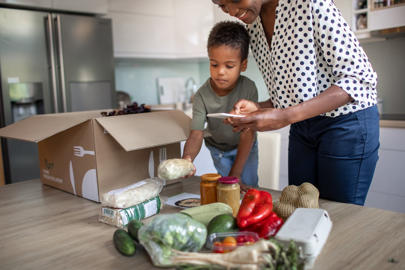 A woman and her son unboxing a meal prep kit they've just received.