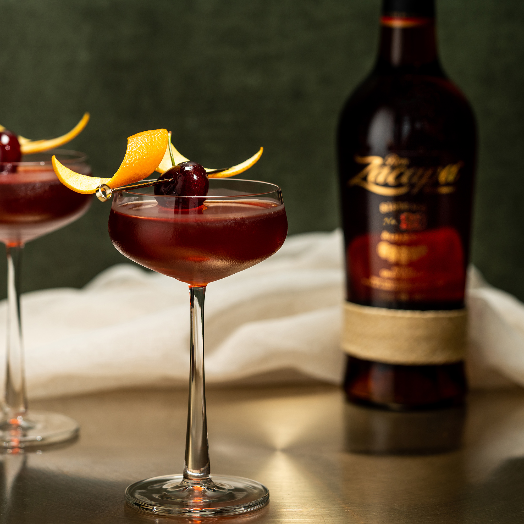 A sophisticated cocktail glass filled with a deep red drink, garnished with an orange peel and a cherry on a skewer.