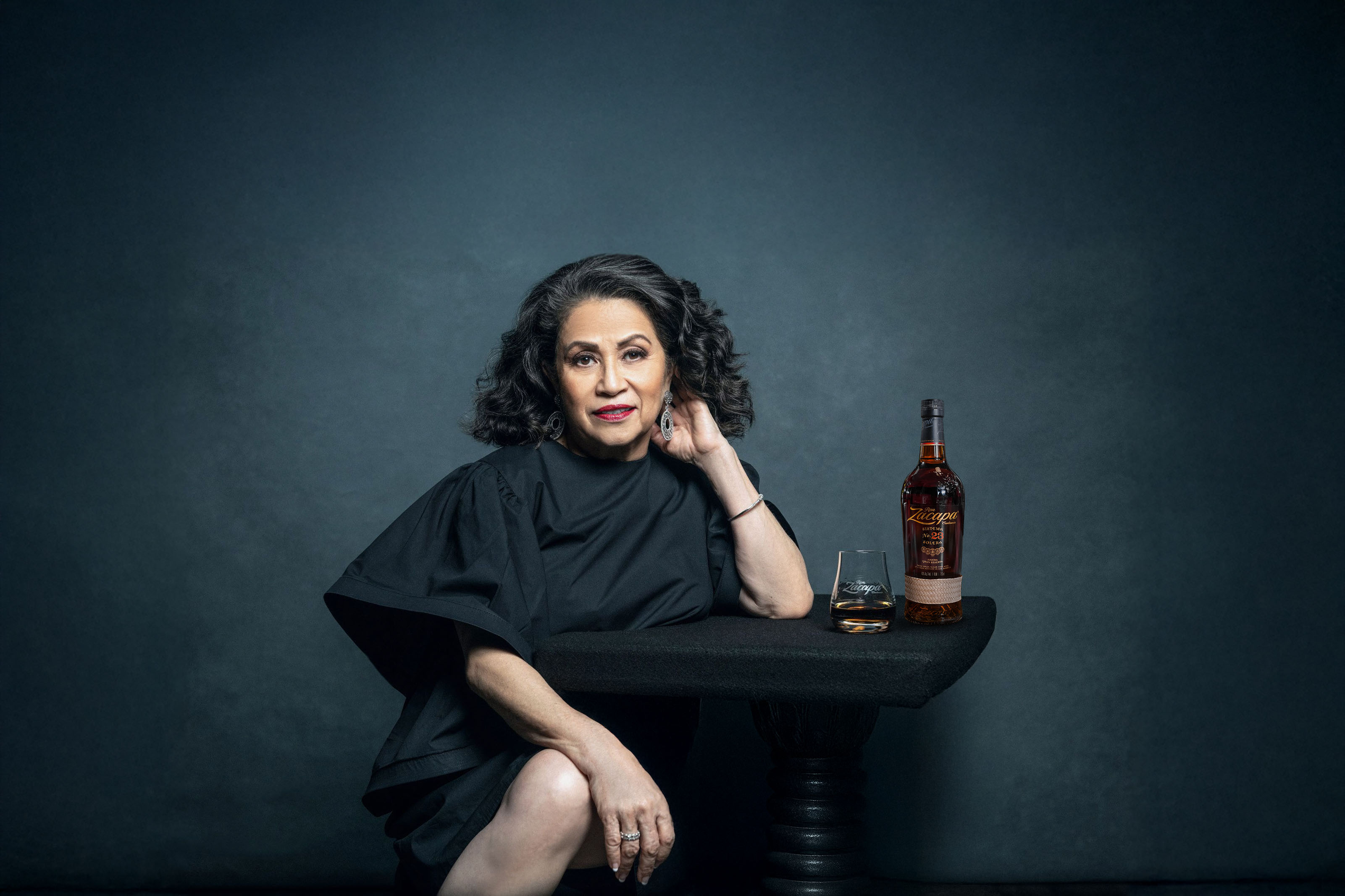 A person seated at a table with a bottle of whiskey and a filled glass.