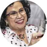 A person wearing a white polka dot shirt and holding a glass of dark liquid.