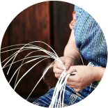 A person wearing a colorful woven garment is skillfully weaving thin, white strands together with their hands.