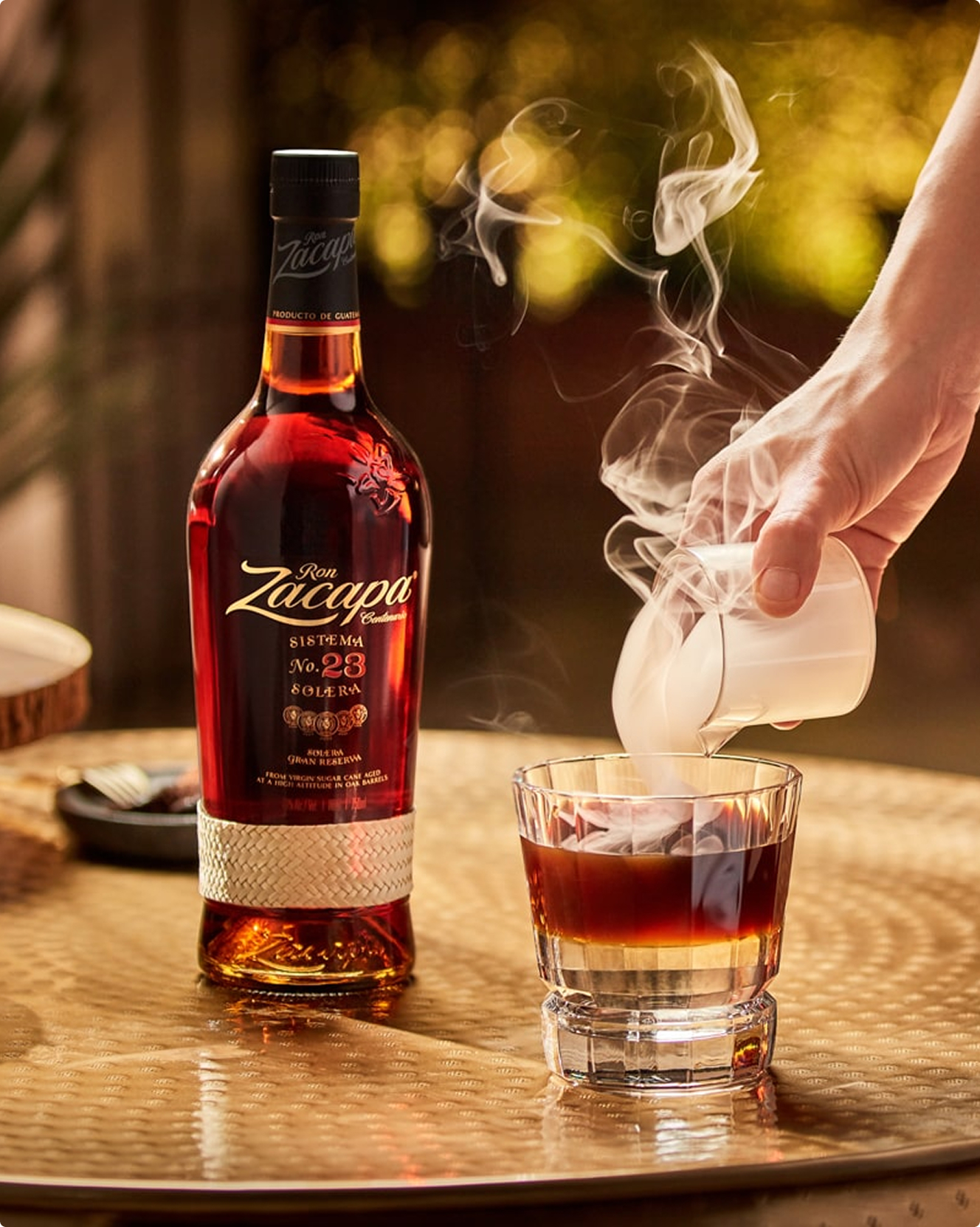 A hand pouring smoke out of a glass over a Carajillo cocktail 
