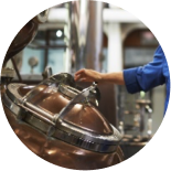 A person wearing a blue shirt is interacting with large copper distillation equipment inside a distillery.