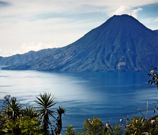 A scenic view of a large, conical mountain next to a calm lake.