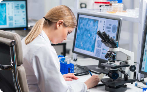 Scientist analyzing data through a microscope and computer screen in a lab.