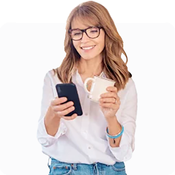Woman smiling at her phone while holding her mug.