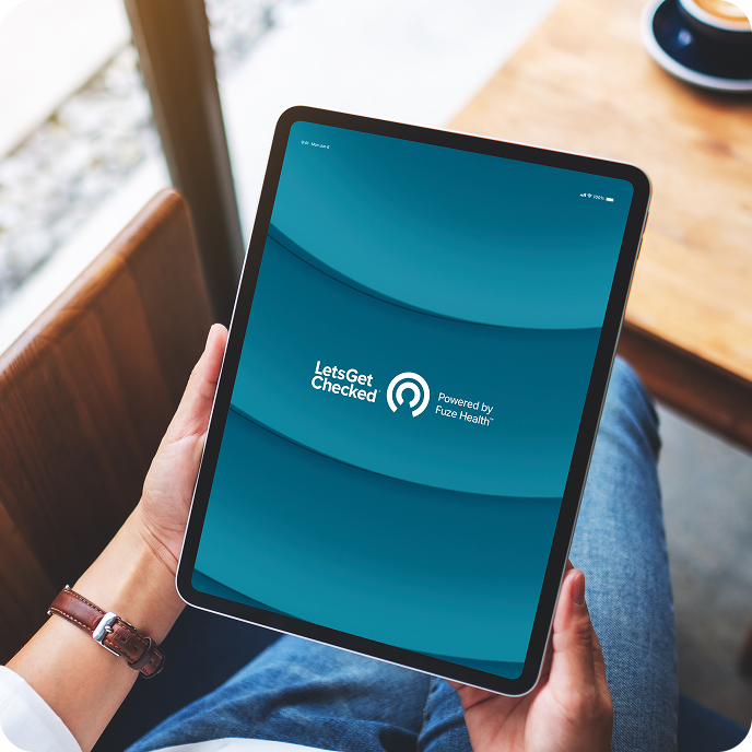 Person holding a tablet displaying the LetsGetChecked logo with the text "Powered by Fuze Health."