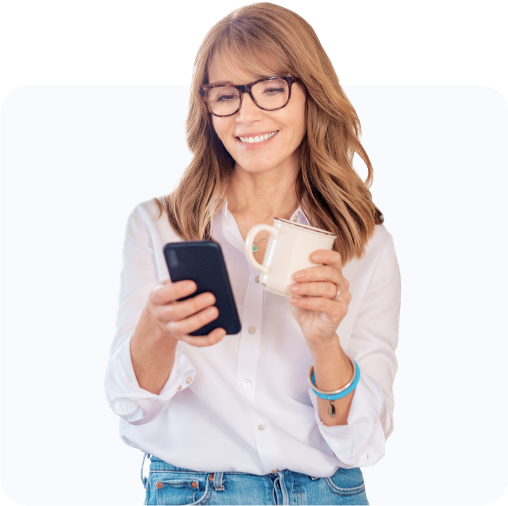 Woman smiling at her phone while holding her mug.