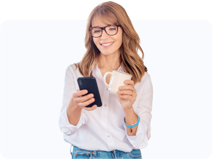 Woman smiling at her phone while holding her mug.