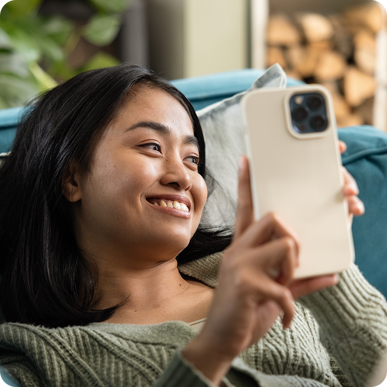Woman smiling while using her phone on a sofa.