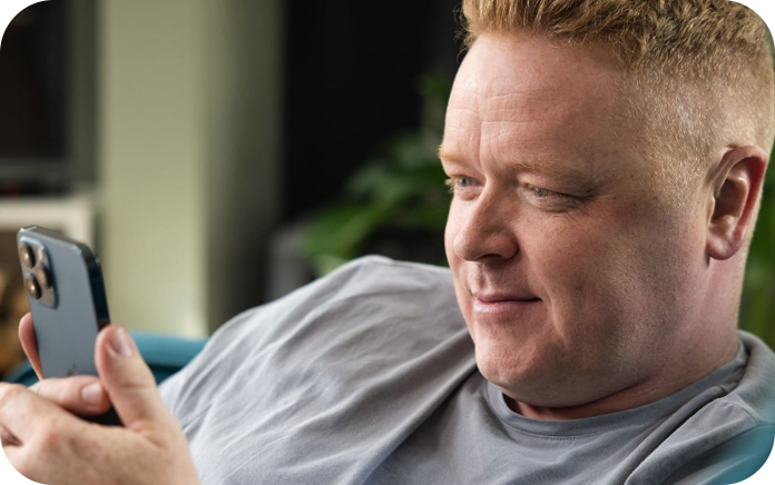 Man sitting on a couch, looking at his phone and smiling.