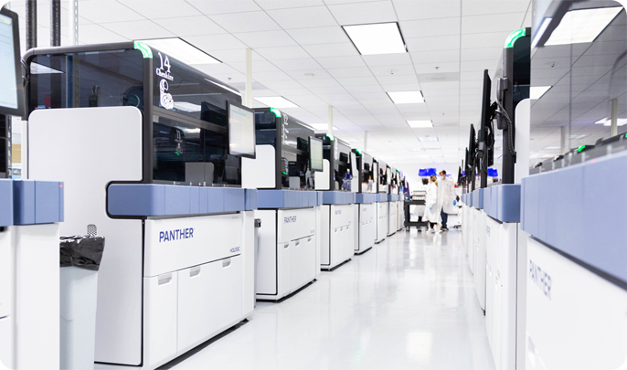 Modern LetsGetChecked laboratory with rows of automated testing machines and ab staff in the distance.