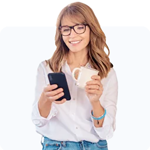 Woman smiling at her phone while holding her mug.