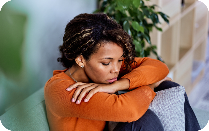 Woman sitting on a couch, with her head resting on her arms, appearing tired or stressed.